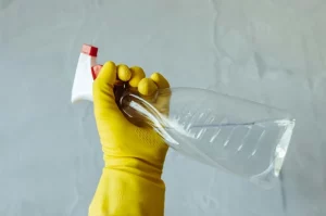 personne avec un gant de nettoyage jaune et un produit